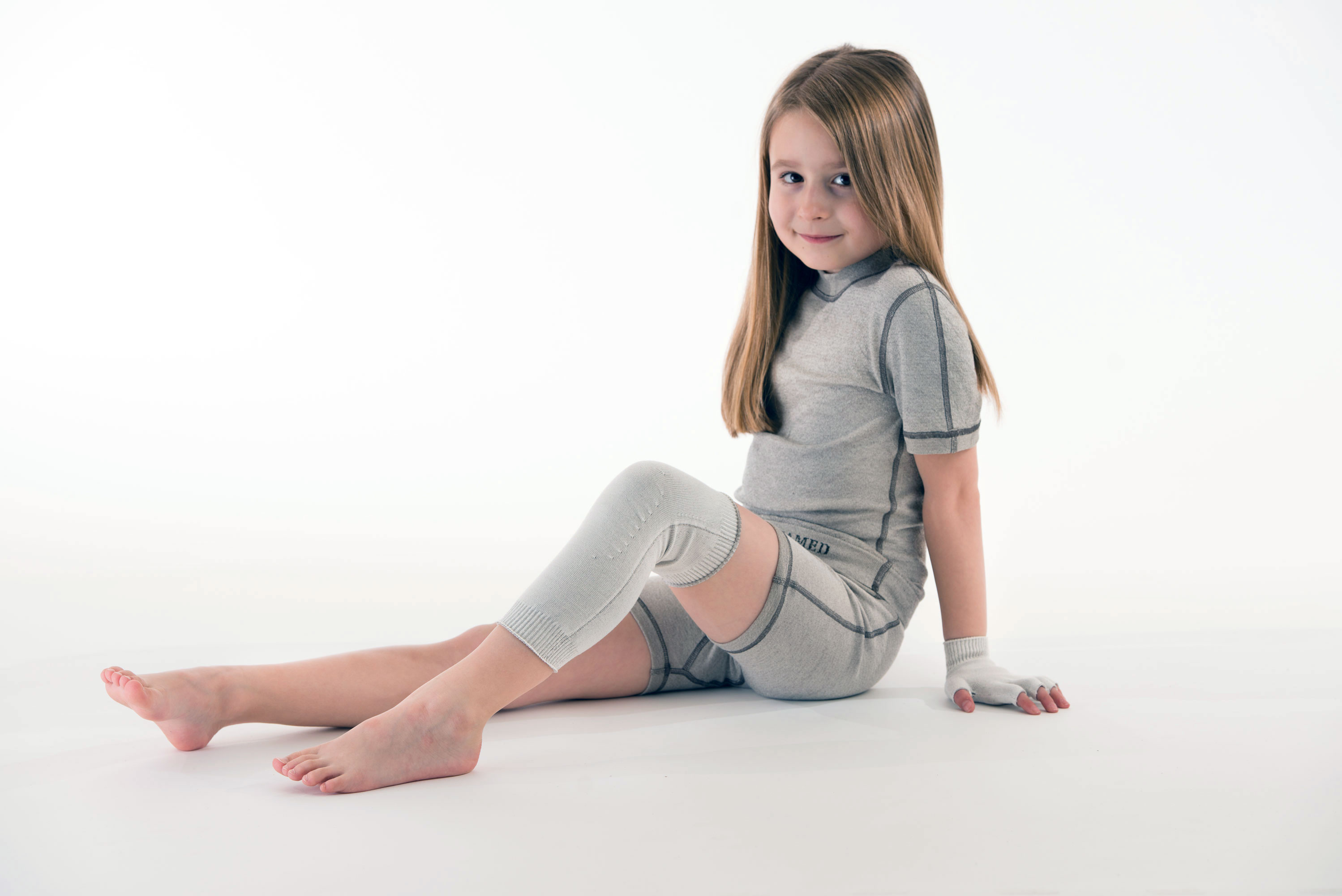 KK_KniestulpenT3icsr6hvDG4M Mädchen mit Kniestrümpfen, Fingerhandschuhen und kurzem Overall aus Silbertextilien auf neutralem Hintergrund – hautfreundlich, atmungsaktiv und juckreizlindernd.